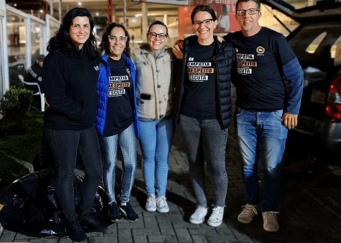 Equipe de voluntários da Associação Nós na Rua reunida durante ação social, com caixas de doação.