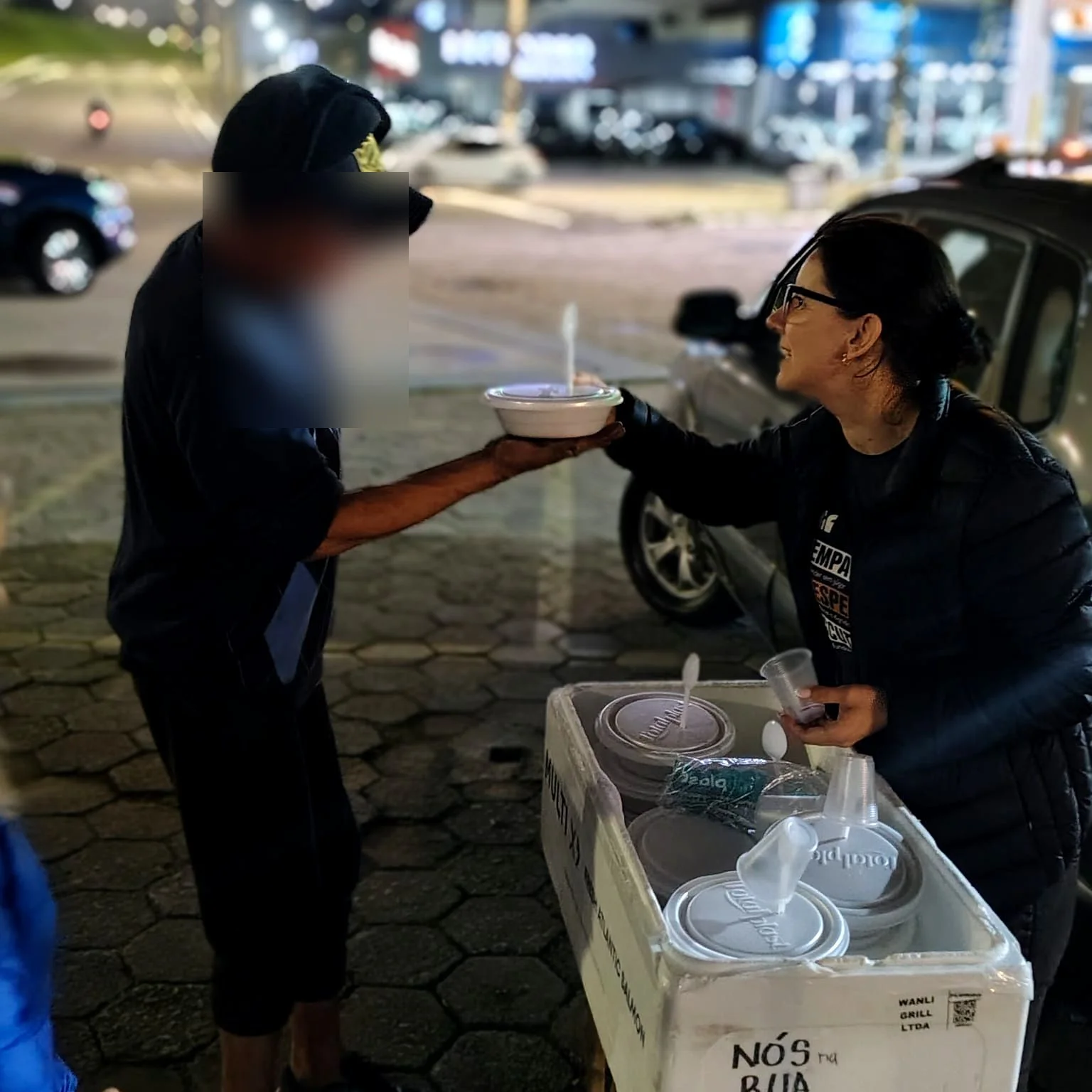 Voluntária do Nós na Rua entregando uma marmita durante ação noturna.